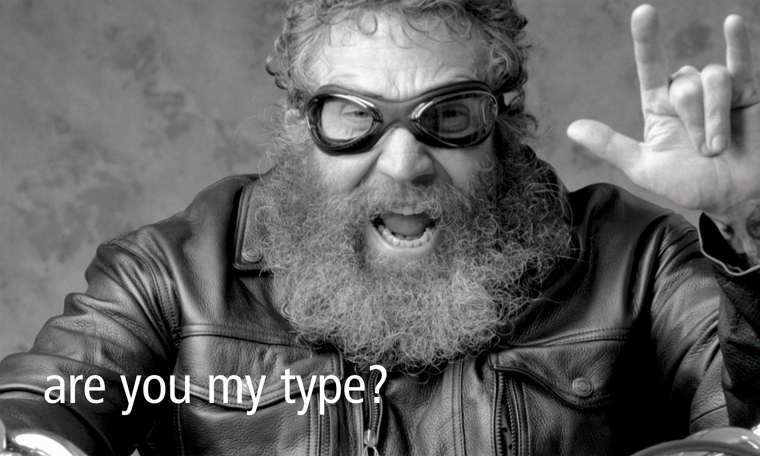 Bearded man with goggles gesturing expressively in black and white photograph.